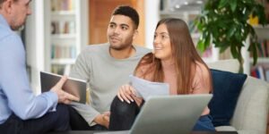 A young couple sitting at a table and smiling while reviewing financial charts and documents with a professional female advisor.
